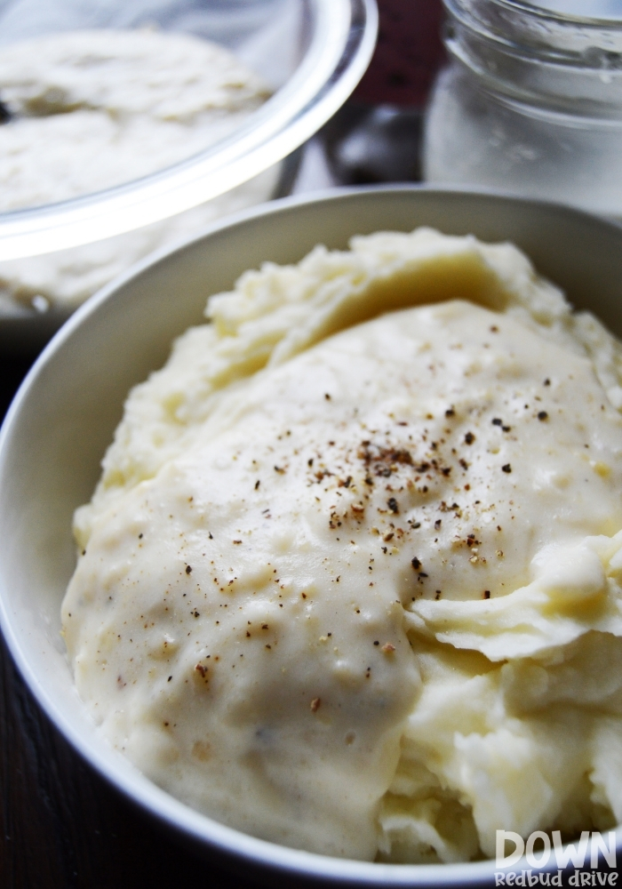 Tall picture of white gravy on mashed potatoes in a white bowl.