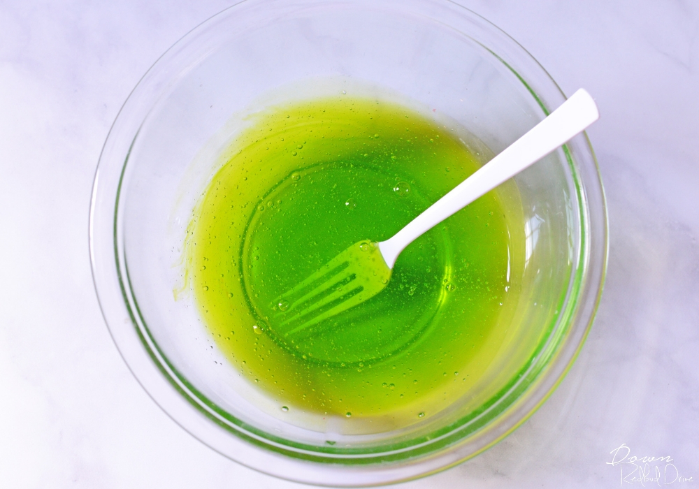 green glue mixture in a clear glass bowl with a white plastic fork