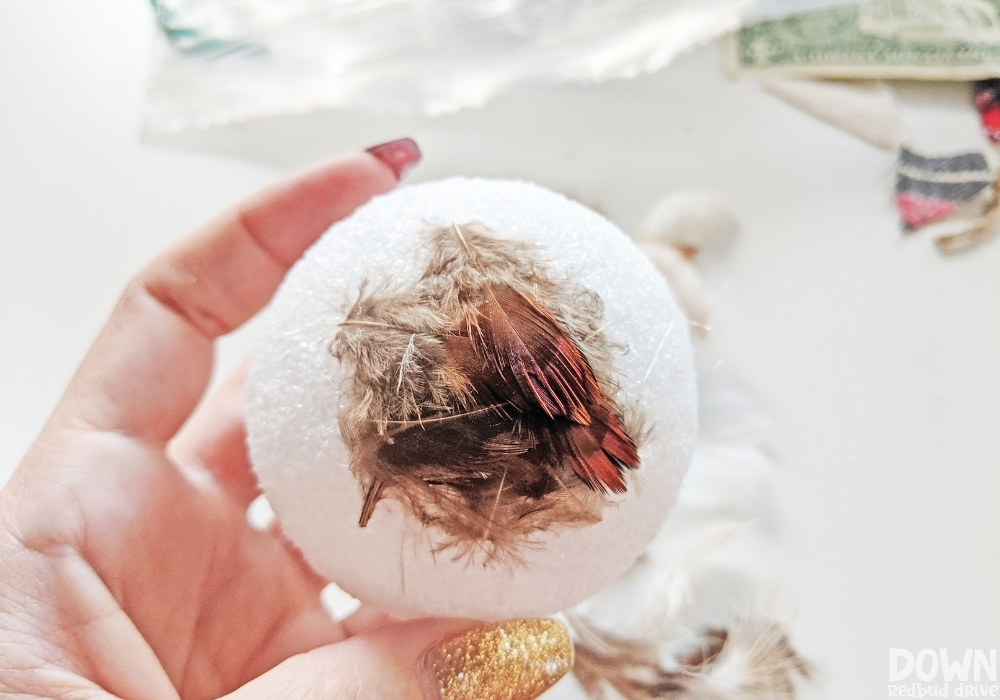 Close up of feathers being attached to a foam ball.