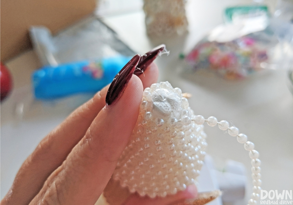 Up close picture of a pearl strand being wrapped around the top of a foam Christmas tree form.