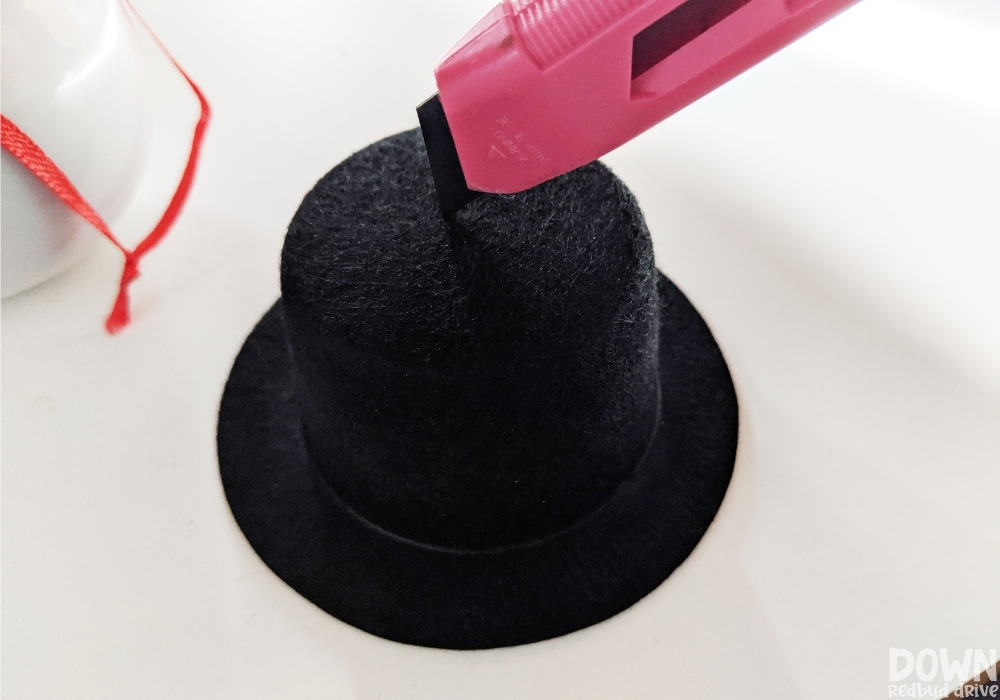 Close up of a hole being cut in a small felt top hat with a box knife .