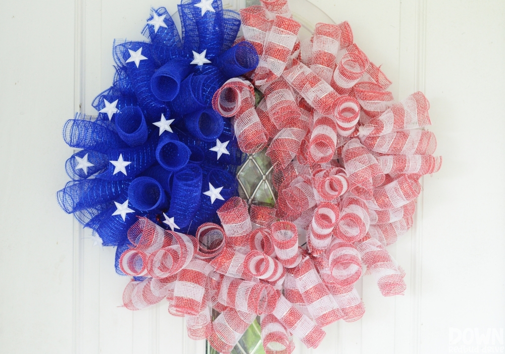 The finished DIY American Flag Mesh Wreath hanging on a wreath hanger on a white door.