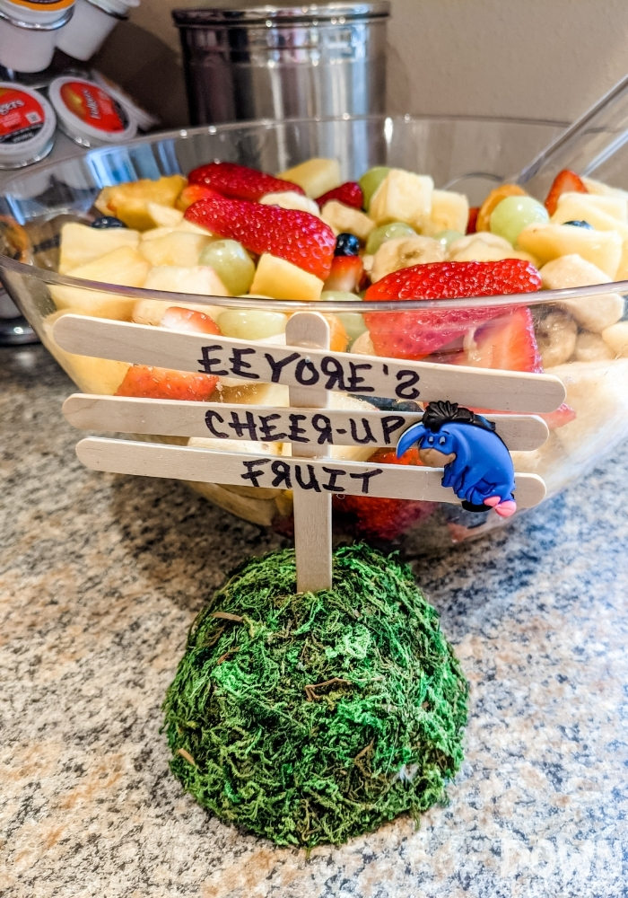 A bowl of fruit with a sign that says "Eeyore's Cheer-Up Fruit".