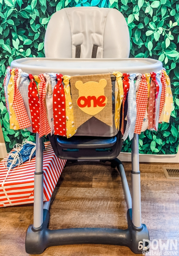 A Winnie The Pooh first birthday banner on a high chair.