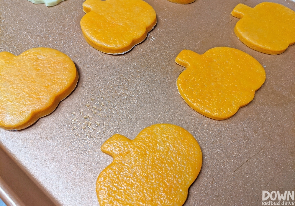 Overhead view of pumpkin shaped sugar cookies on a cookie sheet.