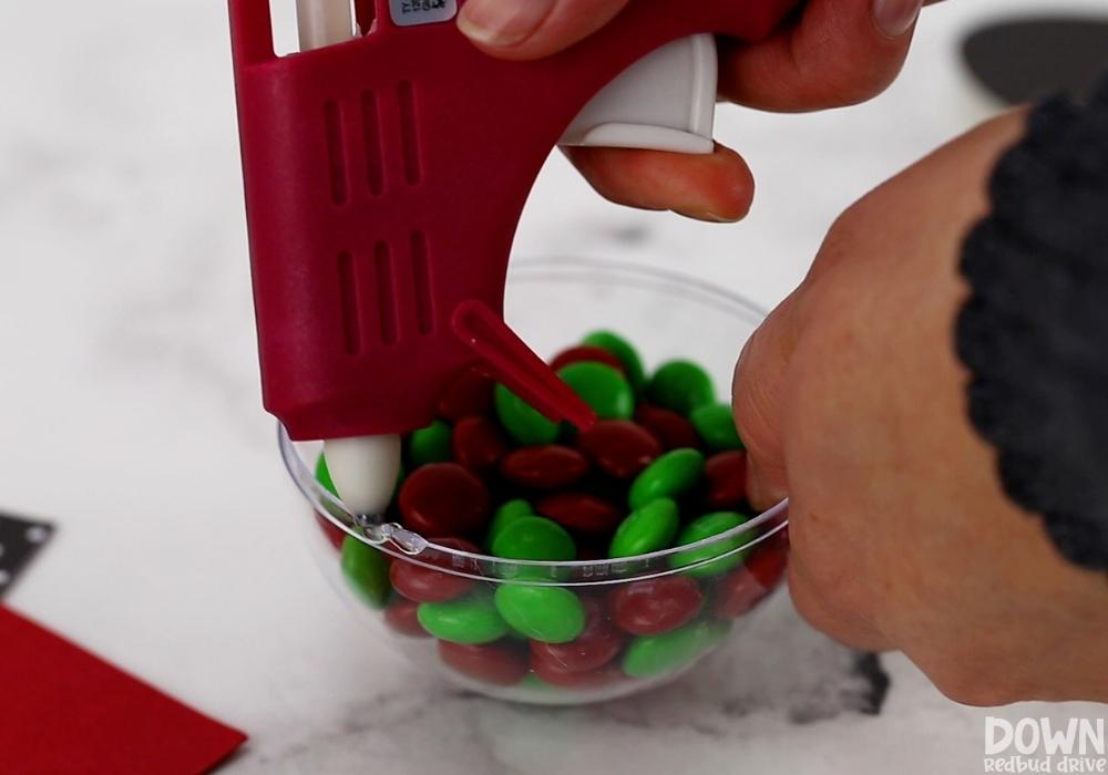 Glue being added to a plastic dome full of M&Ms to add a printable to.