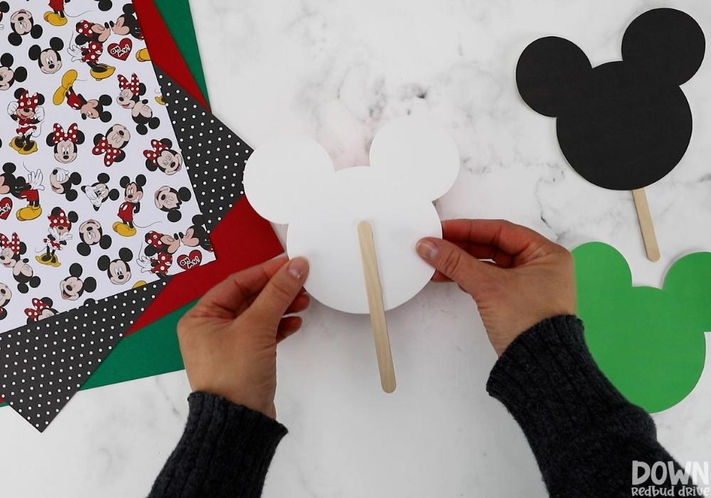 A popsicle stick hot glued to a mickey mouse head cutout.