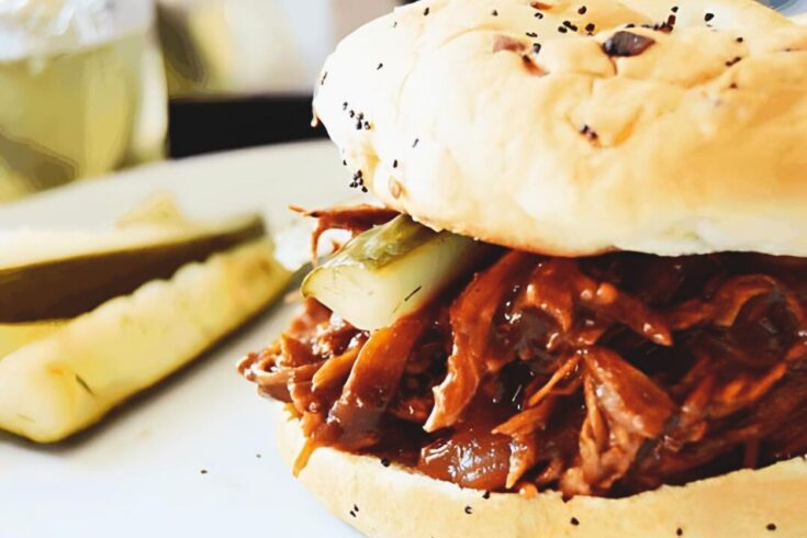Finished crockpot bbq chicken sandwich on a white plate with several pickle spears next to it.