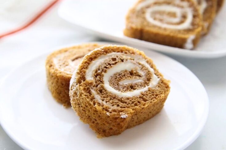 2 slices of homemade pumpkin roll cake on a white plate, additional slices in the background