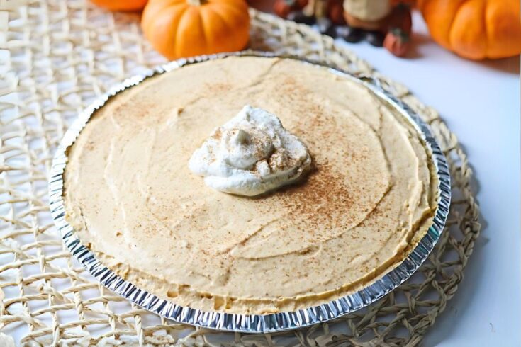 Finished no-bake pumpkin cheesecake with whipped cream dollop on top, a jute placemat under the pie and mini pumpkins in the background