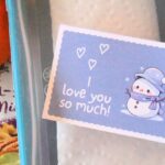 close up of a printable winter lunch box note with the words I love you so much and a cute snowman inside a packed kids school lunchbox.