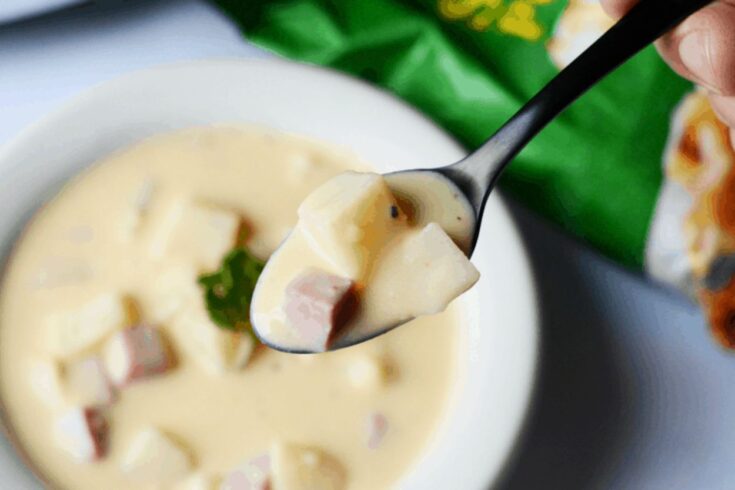 close up of a spoon of crockpot ham and potato soup with a white bowl in the background.