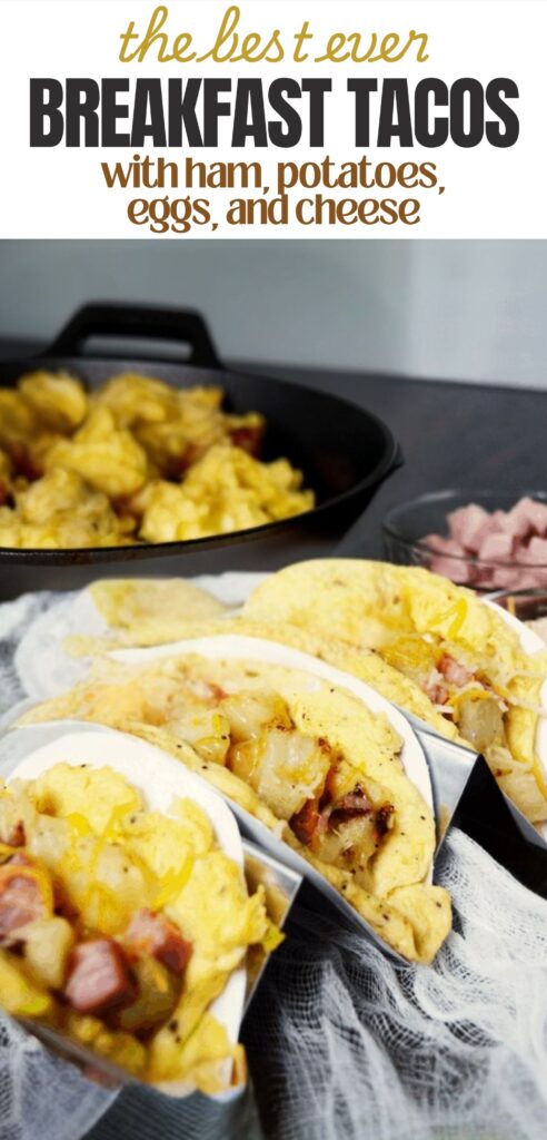 finished breakfast tacos in a taco stand with ham potatoes eggs and cheese with a text overlay that reads the best ever breakfast tacos with ham, potatoes, eggs, and cheese