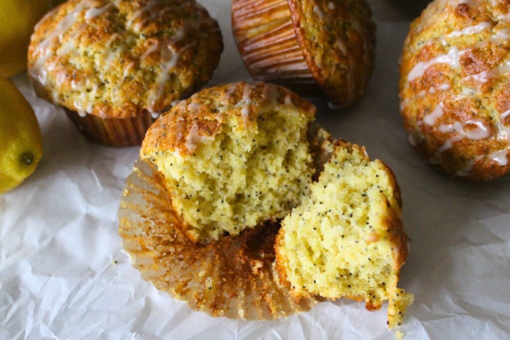 Finished lemon poppy seed muffins in the background, with another cut open to show the interior texture.