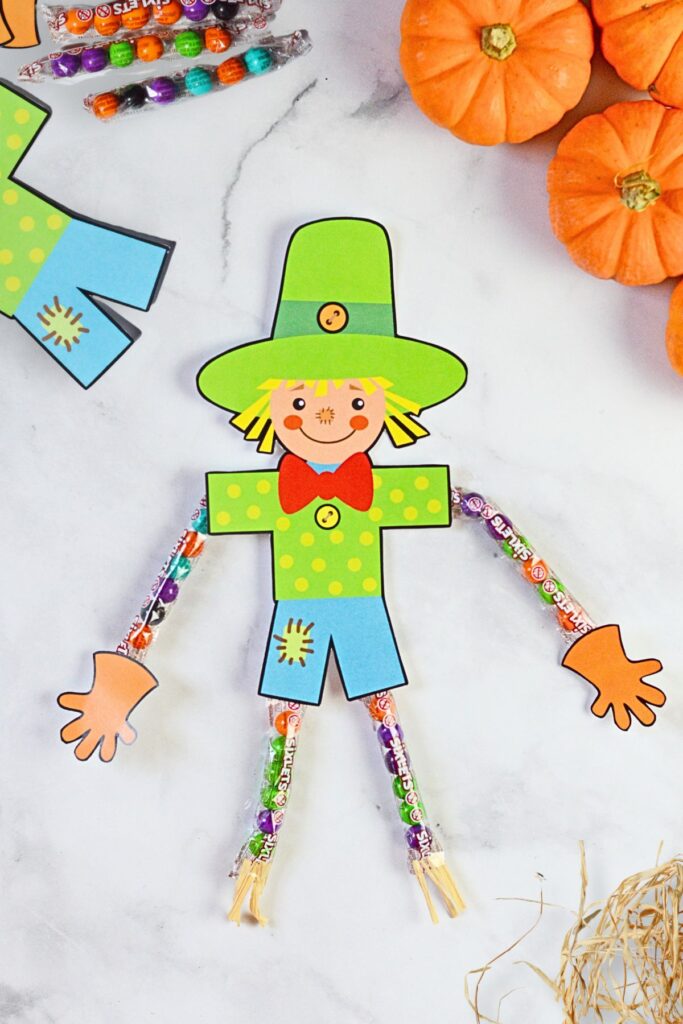 Finished diy sixlets scarecrow with mini pumpkins and extra supplies in the background