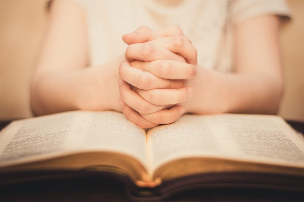 kids hands praying on the bible